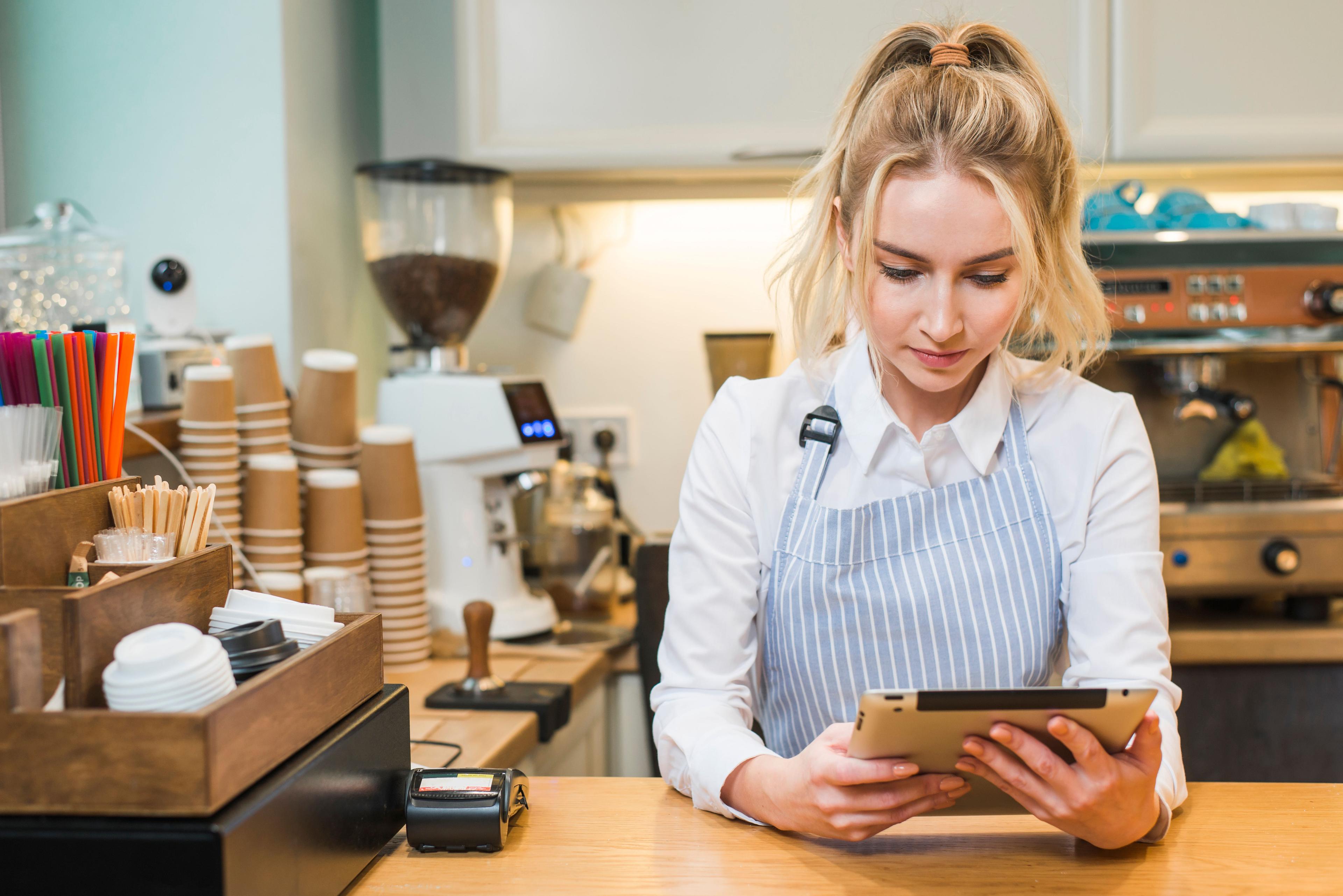 blonde-young-woman-standing-coffee-shop-counter-looking-digital-tablet.jpg
